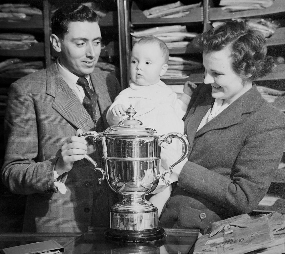 George, Rena and their 10-month-old daughter Margaret with the cup awarded by cloth supplier Keith & Henderson for the “best cut, styled and made occasional jacket”.
